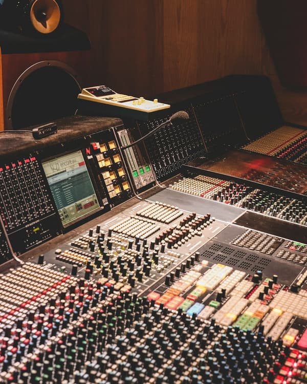 A large analog mixing console in a control room, faders up and no one at the desk.