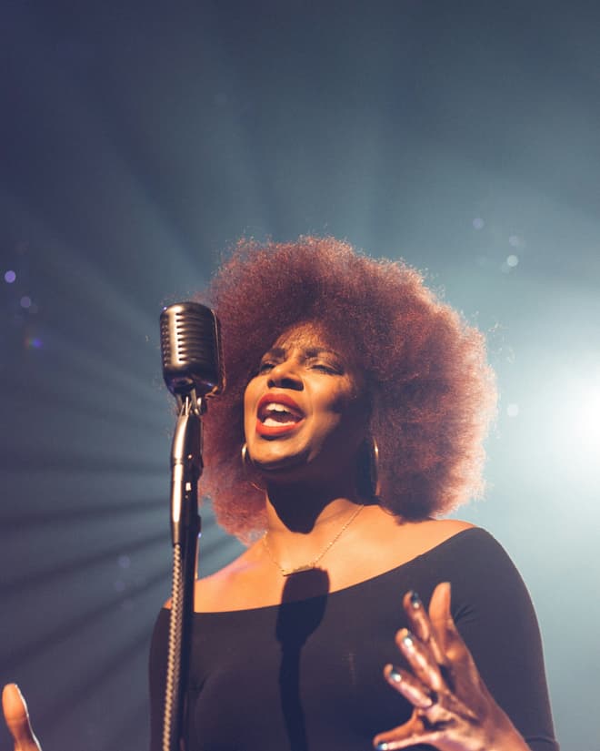 A vocalist singing at a vintage ribbon microphone under a hard white backlight.