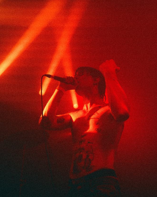 A performer holding a microphone overhead under deep red stage lighting.