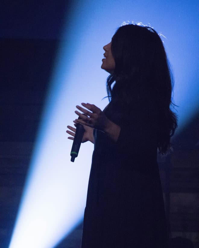 A vocalist in profile against a shaft of blue stage light.